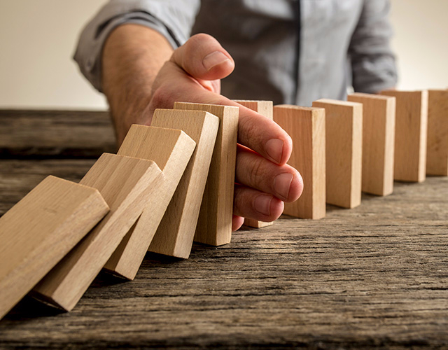 a hand stopping a row of dominos falling.  WD Development can help manage your risk by reviewing your insurance needs